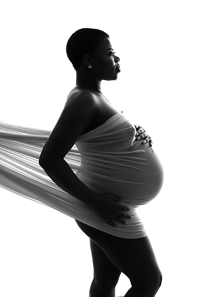 Black and white studio portrait of a pregnant woman wrapped in flowing fabric, taken by a maternity photographer in Richmond, London. Mum posing for a maternity photoshoot in London studio