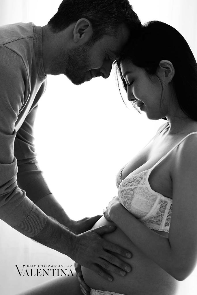 Black and white photo of expecting couple – partner tenderly holding the woman’s bump in a loving third trimester moment.